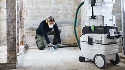 Remeselník brúsi podlahu a používa systém brúsenia podláh Festool s odsávaním.