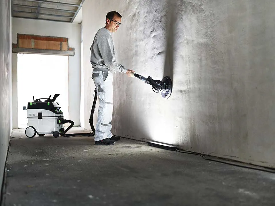 Remeselník osvetľuje stenu pomocou Kontrolného svetla a brúsi ju